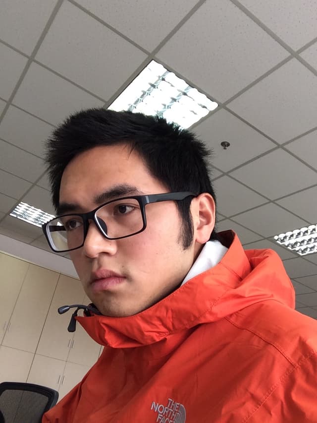 A young Asian man wearing glasses and an orange jacket