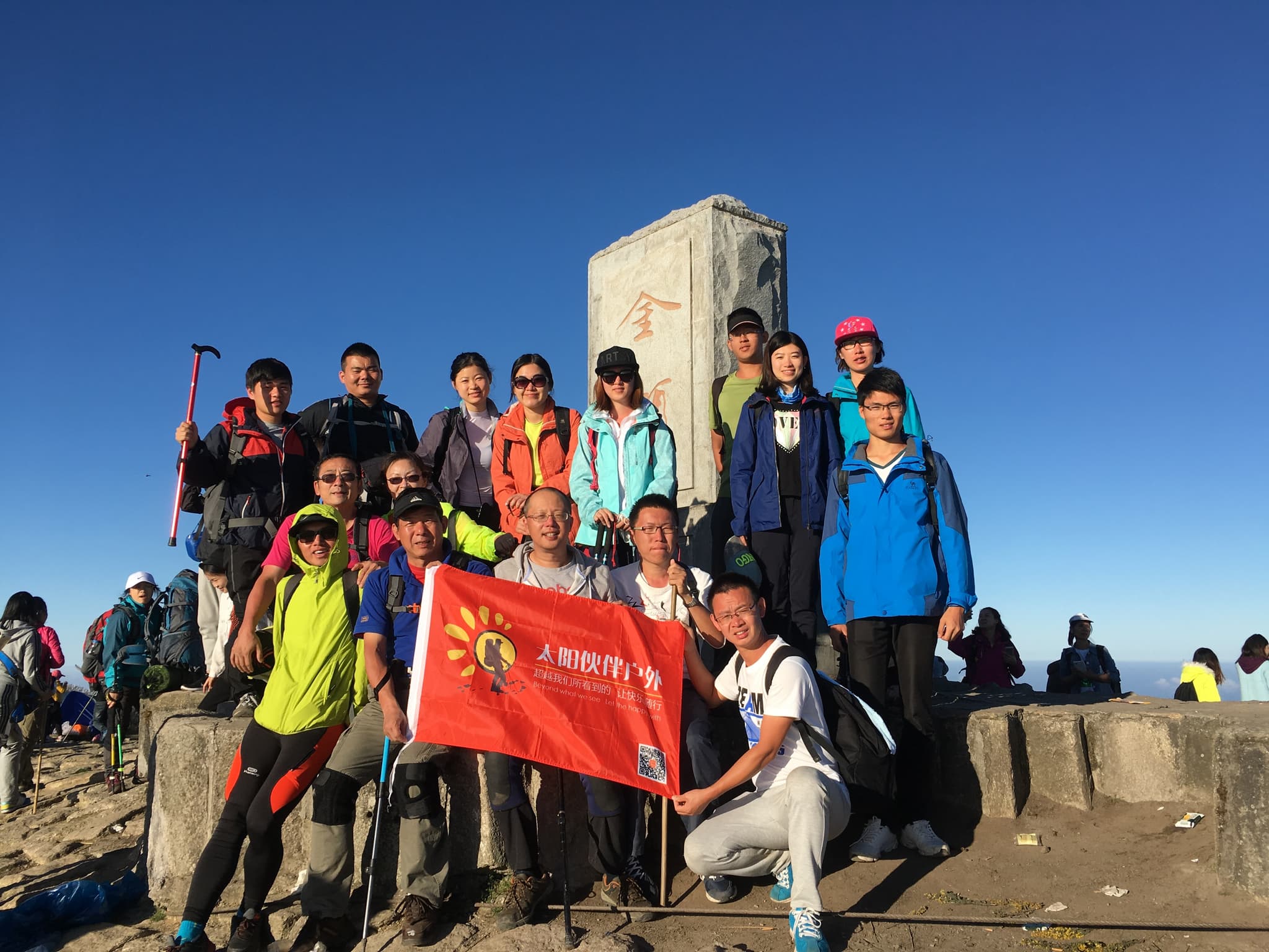 Group of people in jumpsuits and goggles hanging from a bridge with a red flag