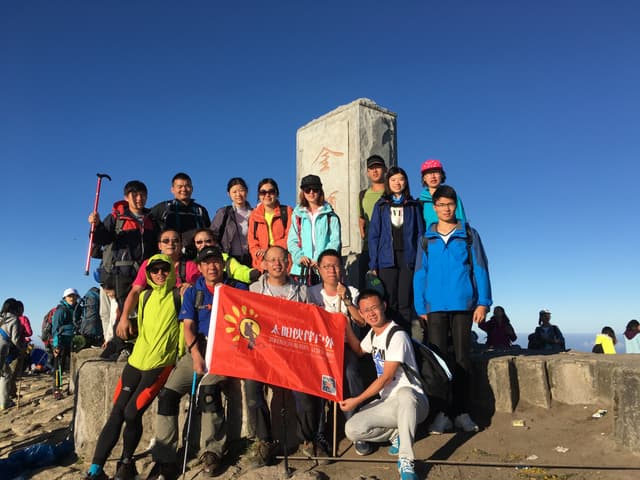 Group of people in jumpsuits and goggles hanging from a bridge with a red flag