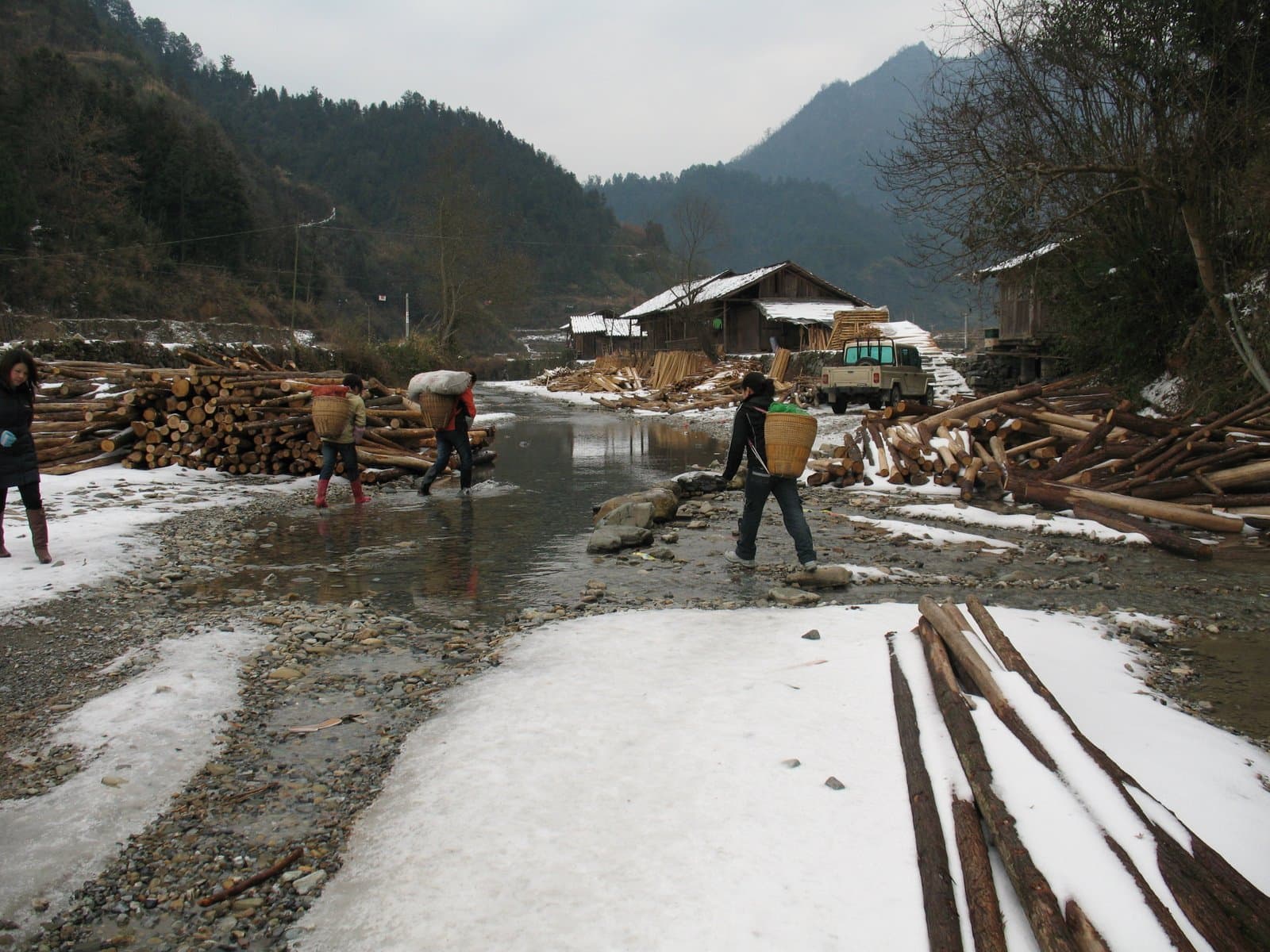 People walking on a muddy snowy road with mountains and debris in the background