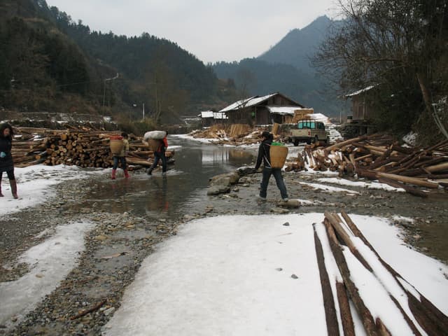 People walking on a muddy snowy road with mountains and debris in the background