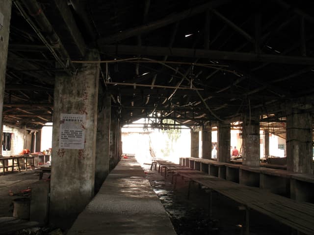 A dimly lit, abandoned walkway with a concrete floor and metal beams