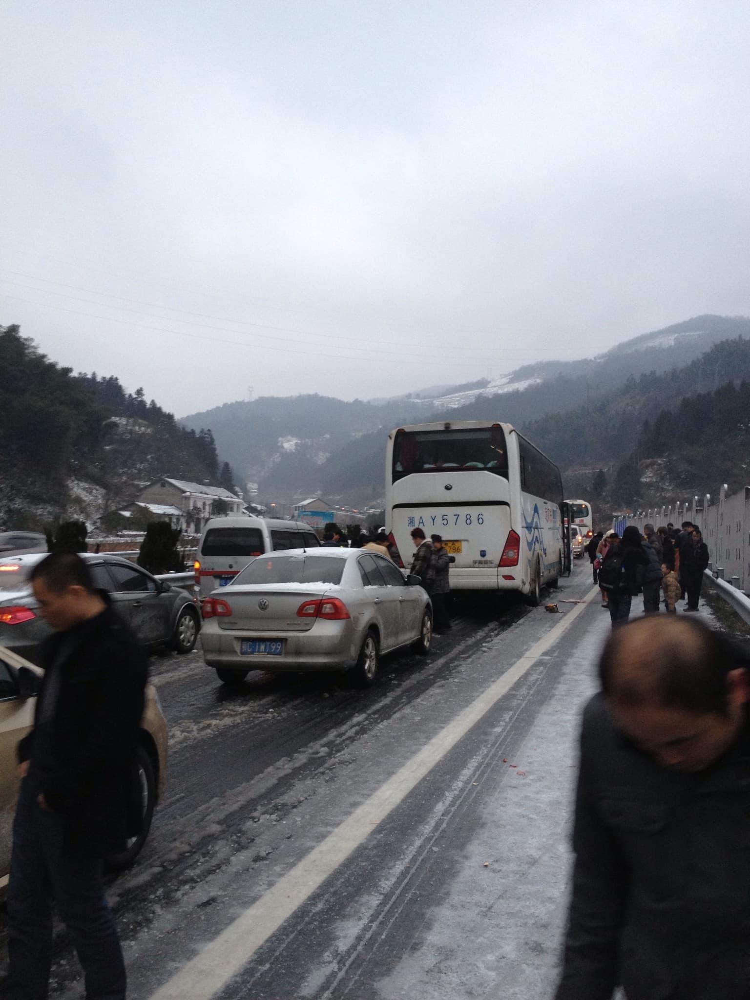 Vehicles lined up on a road with people standing nearby, set against a backdrop of mountains