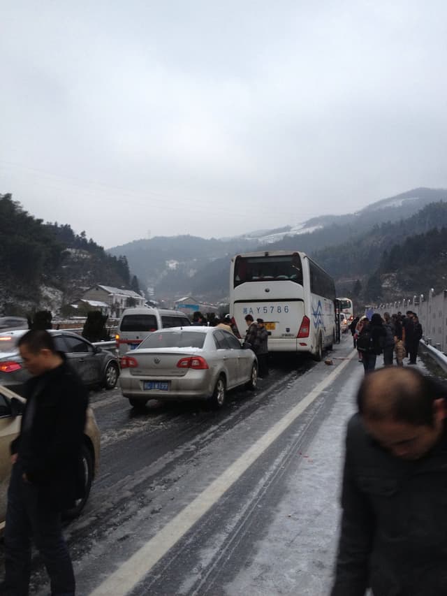 Vehicles lined up on a road with people standing nearby, set against a backdrop of mountains