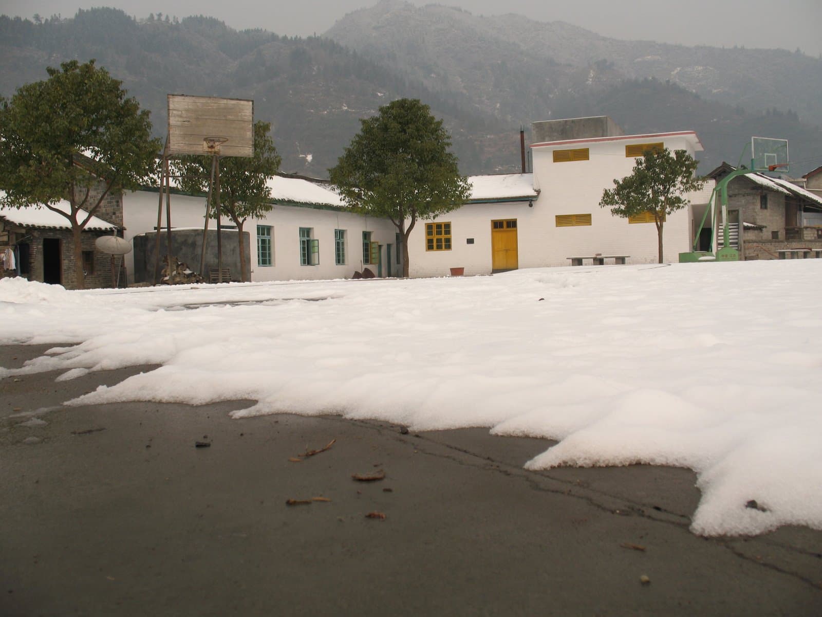 Snow covers the ground in front of a row of white buildings with trees and mountains in the background