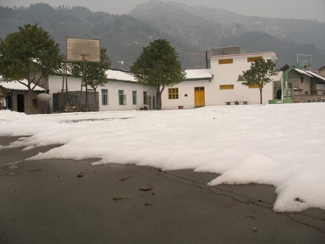 Snow covers the ground in front of a row of white buildings with trees and mountains in the background