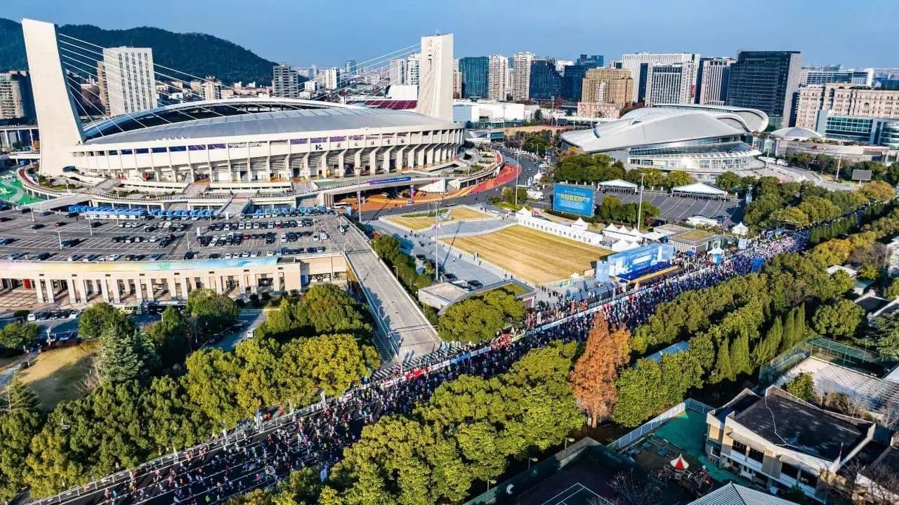 An aerial view of a large stadium surrounded by trees and buildings with a crowd of people