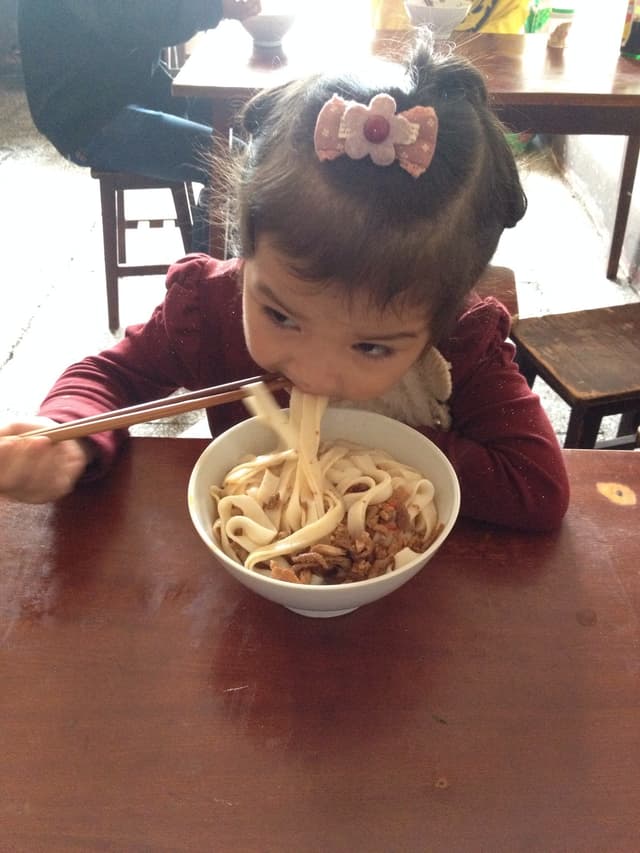 A young girl eating noodles at a table