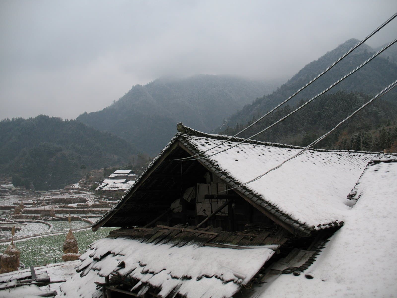 Snow-covered roof of a traditional village building with mountains in the background