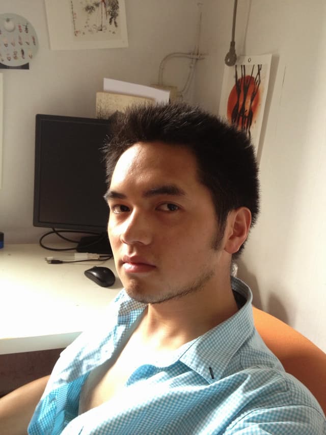 A man sits at a desk with a computer monitor behind him