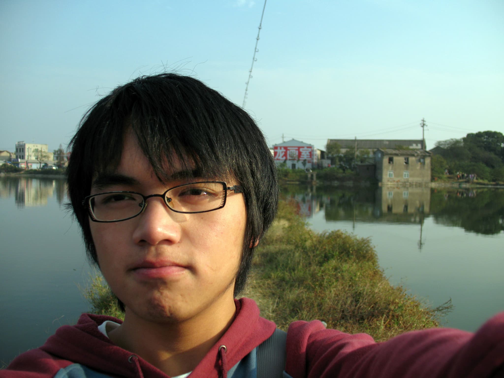 Man taking a selfie by a serene lake with buildings in the background