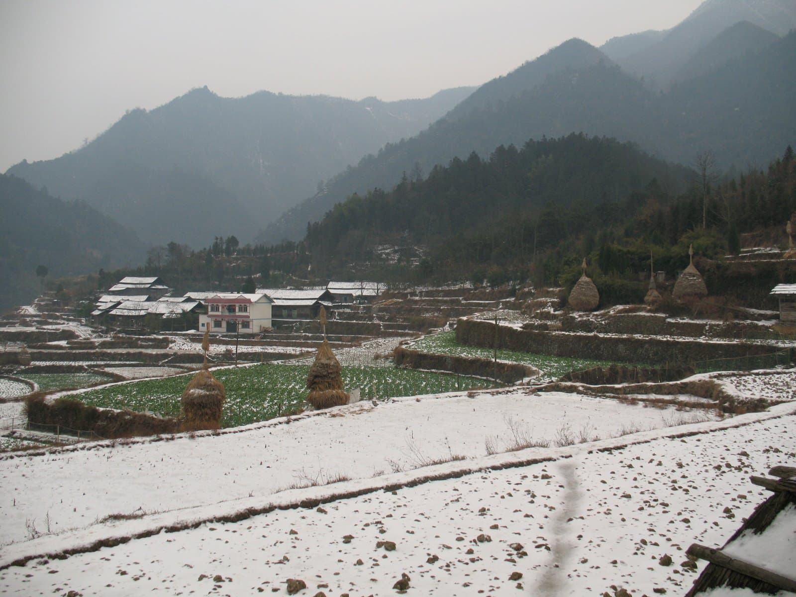 Snow-covered village with terraced fields and mountains in the background