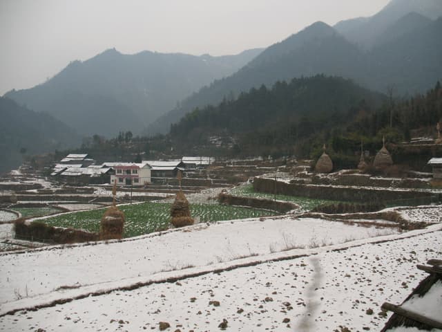 Snow-covered village with terraced fields and mountains in the background