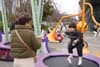 A young child jumping on a trampoline while an adult watches nearby