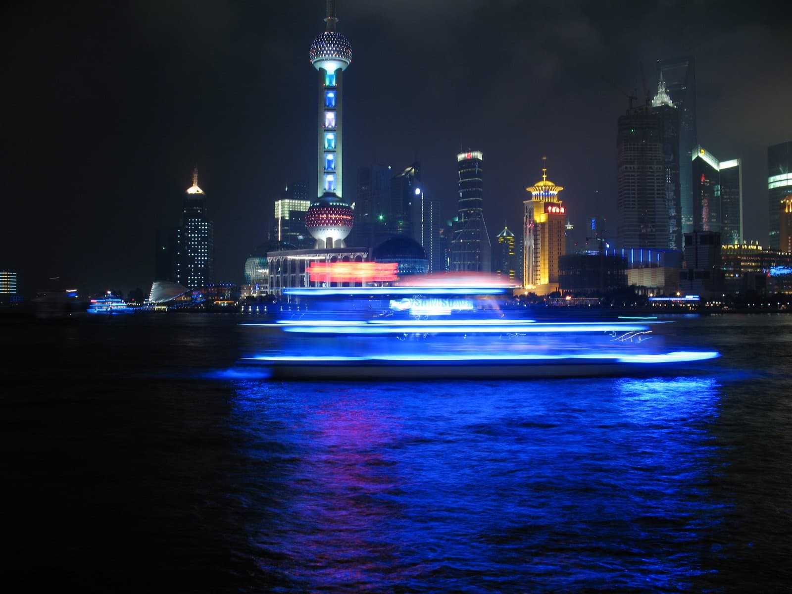 Cruise boat on a river with a city skyline in the background at night