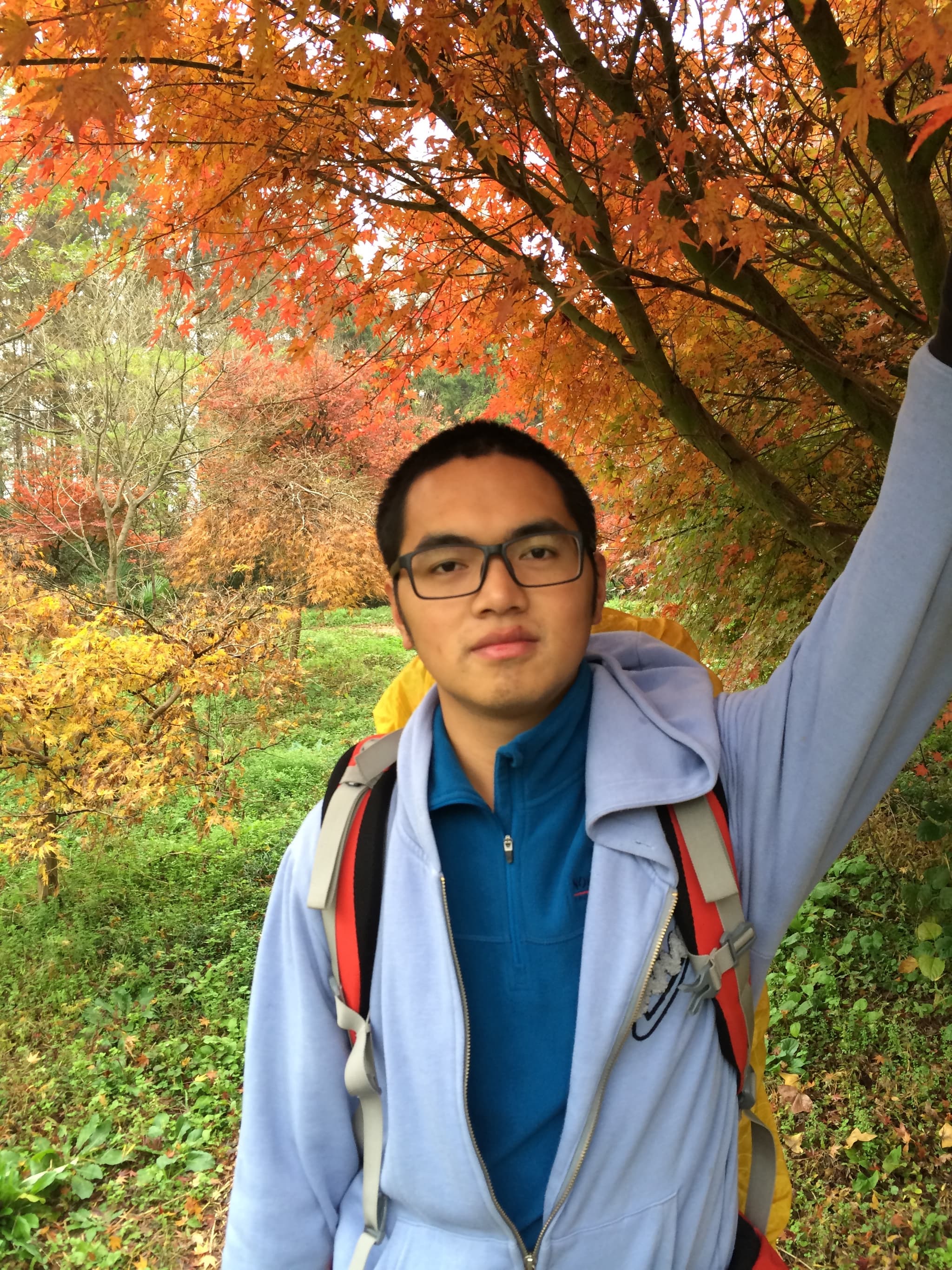 A man stands in front of a tree with colorful autumn leaves