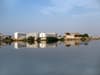 A calm lake reflecting buildings under a blue sky