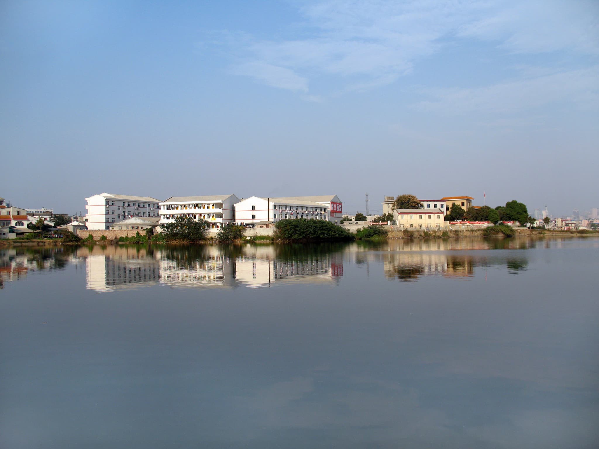 A calm lake reflecting buildings under a blue sky