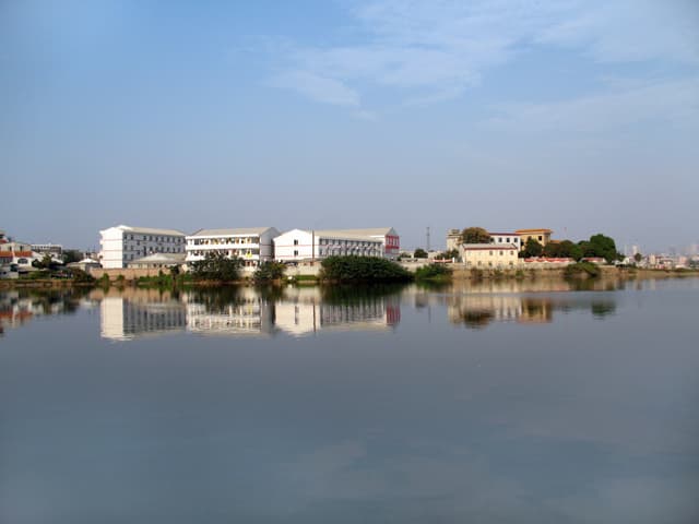 A calm lake reflecting buildings under a blue sky