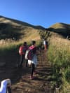 People standing on a dirt path in a grassy field with a hill in the background