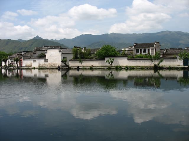 A tranquil village beside a reflective lake with mountains in the background