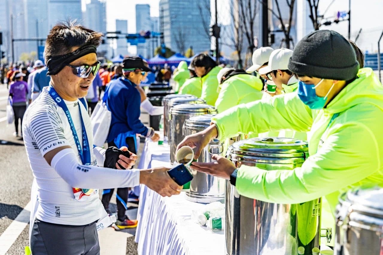 A man receiving a cup of water from a volunteer at a marathon hydration station