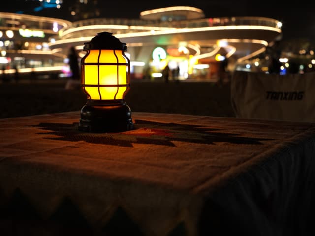 A glowing lantern on a table with a blurred background of a brightly lit building at night