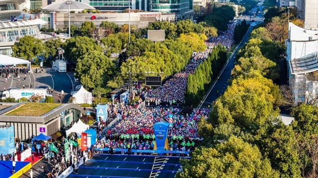 Crowd of runners at a marathon start line surrounded by trees and buildings