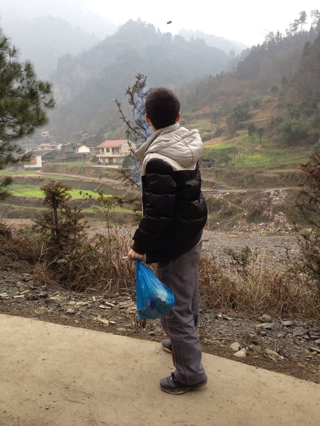 A man walks along a dirt path with a mountainous landscape in the background