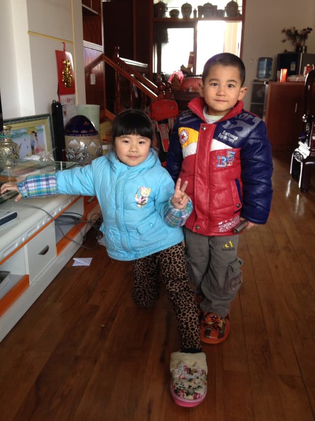 Two children smiling in a room with wooden flooring