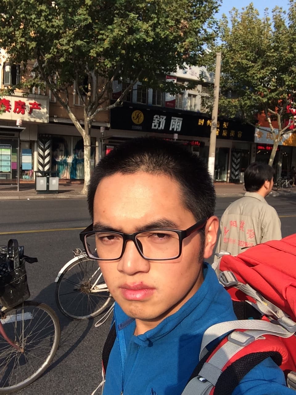 A man with short hair and black glasses smiles at the camera on a city street