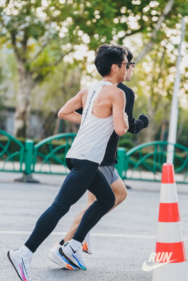 Two men running on a road with a traffic cone
