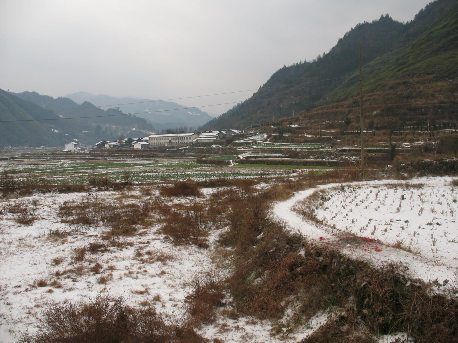 Snow-covered field with a winding path leading to a mountainous landscape