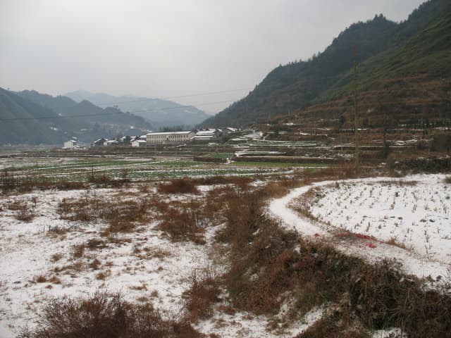 Snow-covered field with a winding path leading to a mountainous landscape