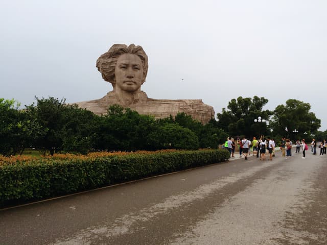 A large stone lion statue standing on a reflective surface with people and trees in the background