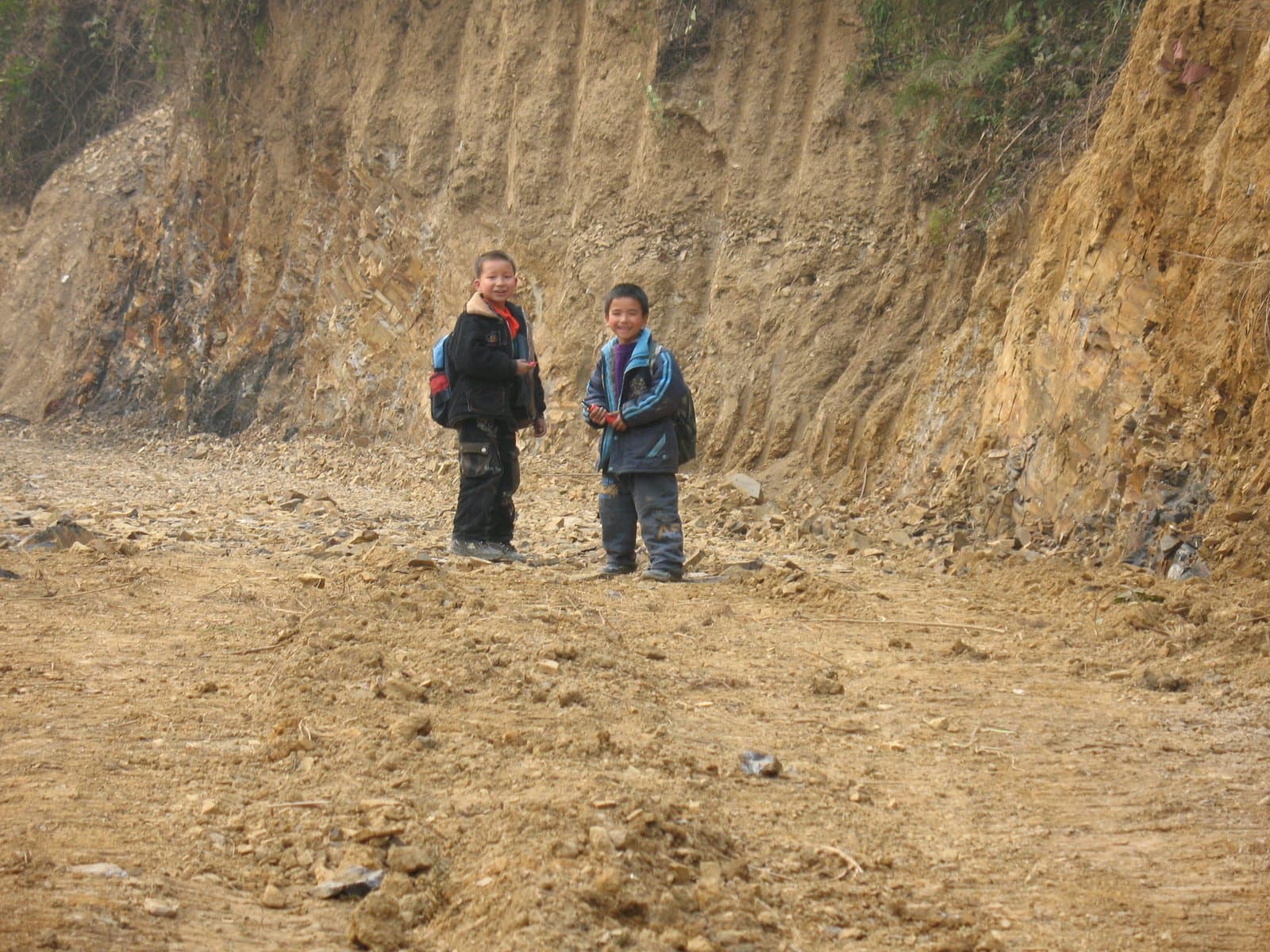 Two people standing on a dirt trail in front of a large cliff