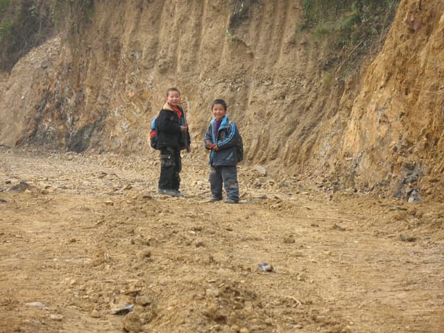 Two people standing on a dirt trail in front of a large cliff