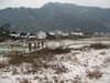A snowy field with people walking in the distance, a village and mountains in the background