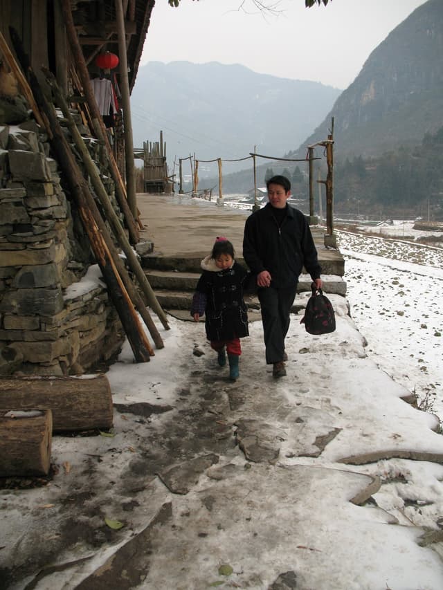 A man and child walking on a snowy path in a mountainous village