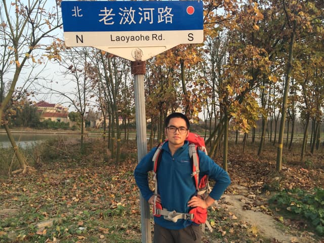 Man with backpack standing beside a directional signpost on a wooded trail