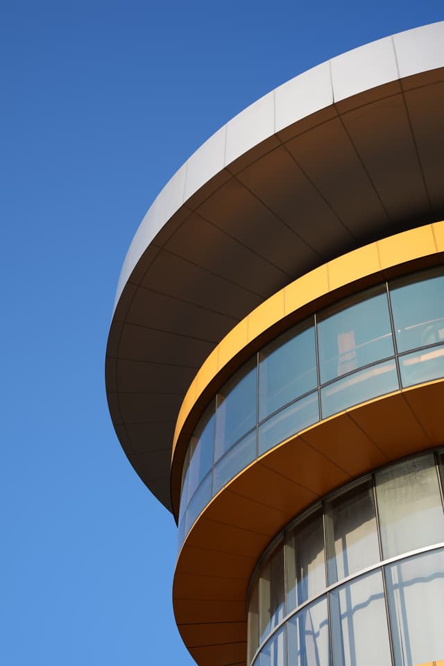 a close-up of a modern building's rounded corner with a large overhang and glass windows against a clear blue sky