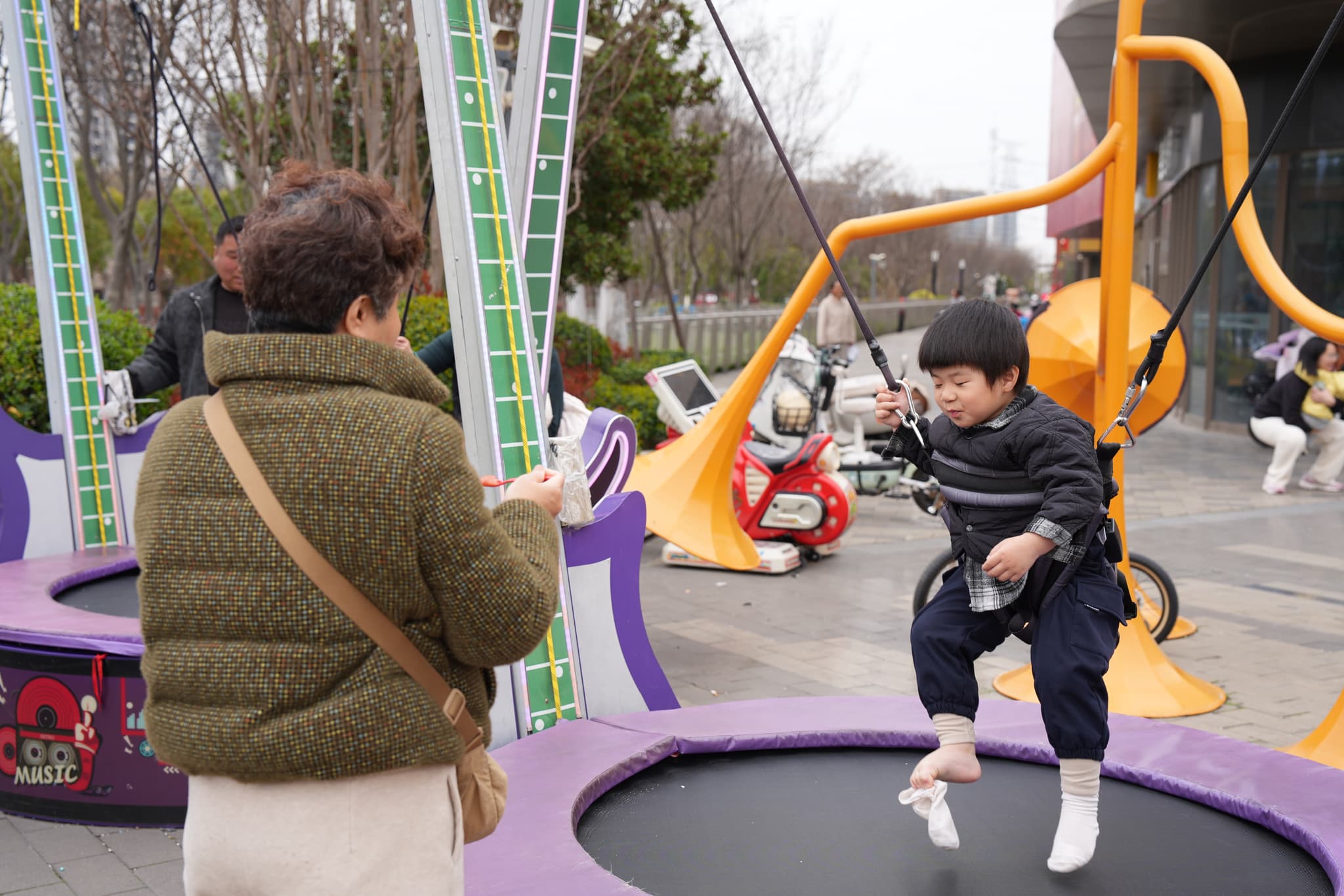 A young child jumping on a trampoline while an adult watches nearby